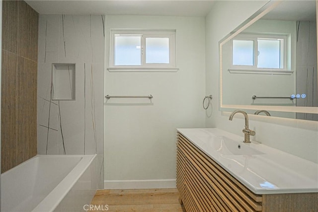 full bathroom featuring baseboards, wood finished floors, vanity, and a healthy amount of sunlight