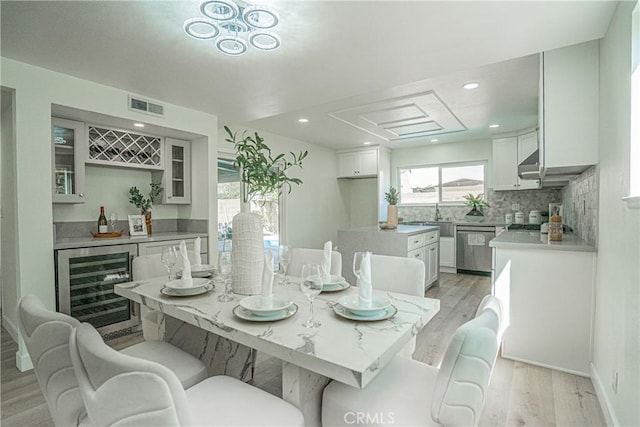 dining room featuring a bar, beverage cooler, light wood-style floors, and visible vents