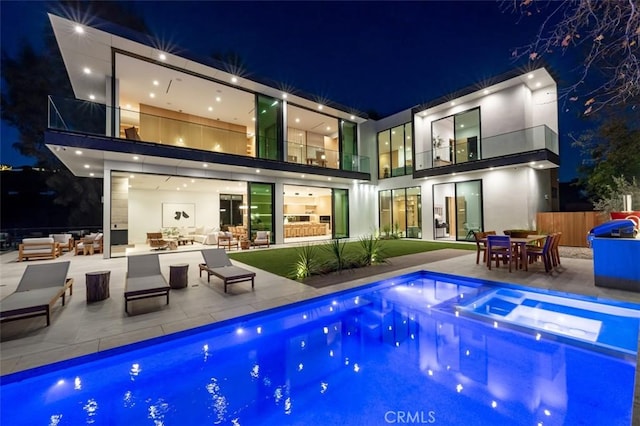 back of house at twilight with a patio area, an outdoor pool, outdoor dining space, and a balcony