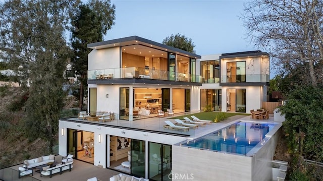 rear view of property featuring outdoor lounge area, a balcony, stucco siding, a patio area, and an infinity pool
