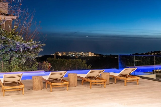 pool at night featuring an infinity pool and a deck