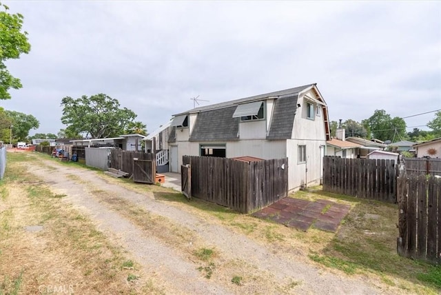 view of side of home featuring fence, a gambrel roof, and roof with shingles