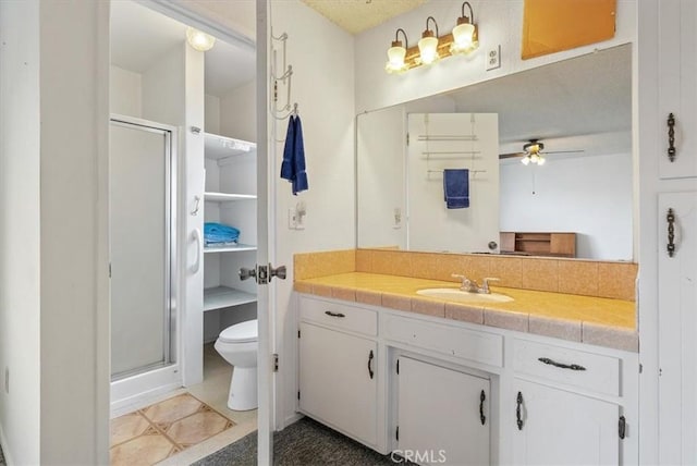 bathroom featuring ceiling fan, toilet, vanity, and a stall shower
