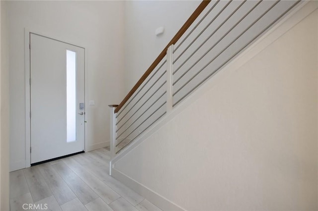 foyer featuring baseboards, light wood-style flooring, and stairs