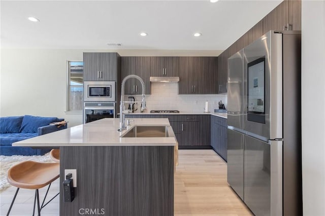 kitchen with a sink, appliances with stainless steel finishes, light countertops, under cabinet range hood, and a breakfast bar area