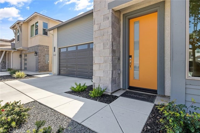 entrance to property with stone siding, an attached garage, and driveway