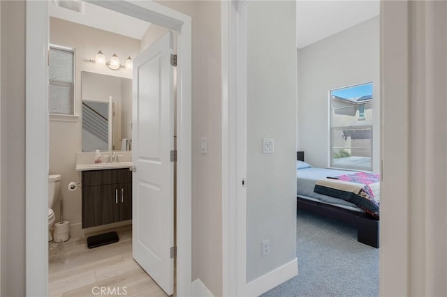 hall with light wood-style floors, baseboards, and a sink