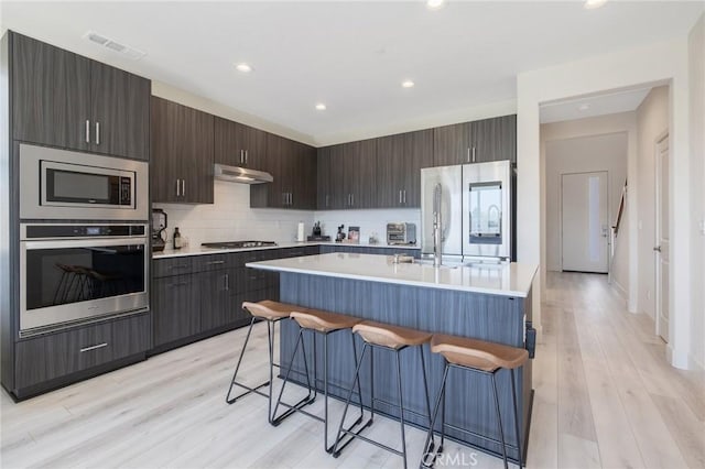 kitchen with visible vents, light countertops, under cabinet range hood, a breakfast bar, and appliances with stainless steel finishes