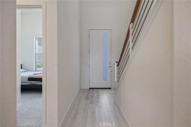 corridor with light wood finished floors, baseboards, and stairs