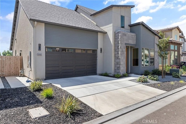 contemporary house featuring concrete driveway, fence, an attached garage, a shingled roof, and stucco siding