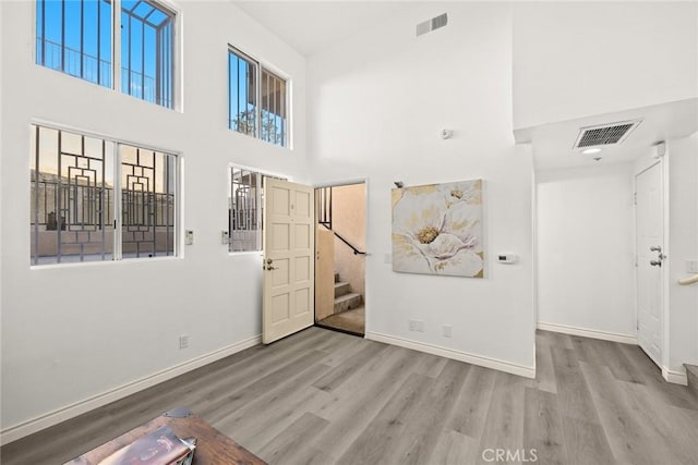 foyer entrance featuring stairway, a towering ceiling, wood finished floors, visible vents, and baseboards