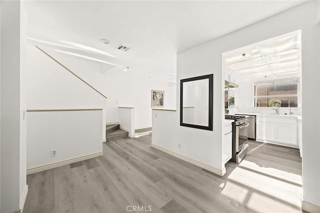unfurnished living room with a sink, stairs, light wood-style floors, baseboards, and visible vents