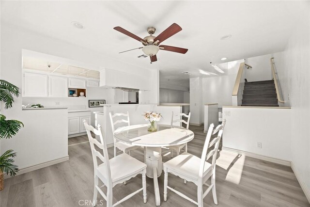 dining area featuring stairs, light wood-style floors, ceiling fan, baseboards, and visible vents