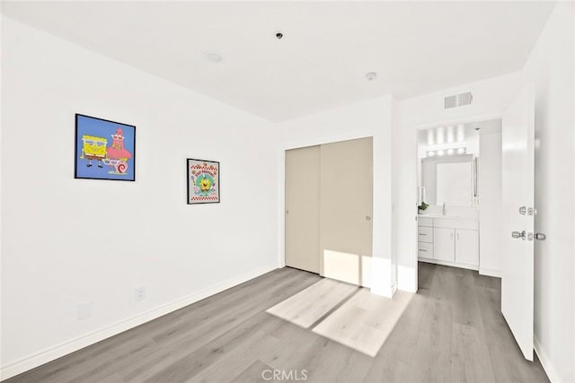 unfurnished bedroom with wood finished floors, visible vents, a sink, a closet, and baseboards