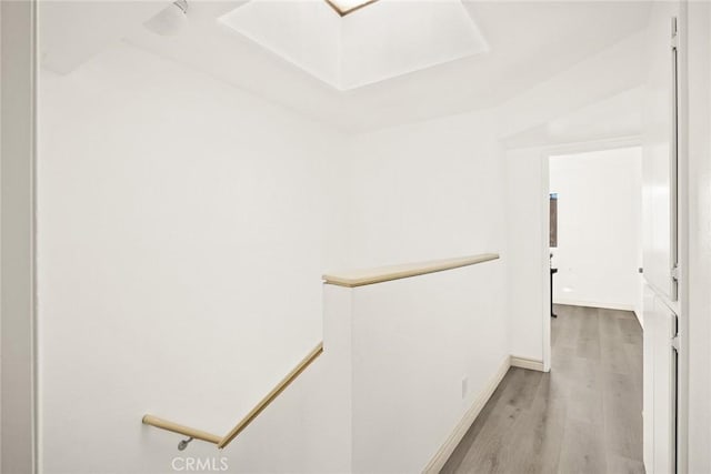 corridor featuring wood finished floors, baseboards, and an upstairs landing