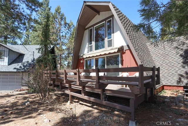 back of property featuring a wooden deck, roof with shingles, and a garage