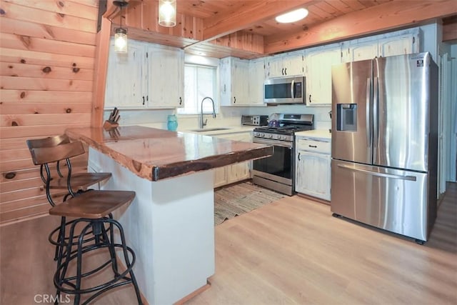 kitchen with stainless steel appliances, a sink, light wood-style floors, a peninsula, and a breakfast bar area