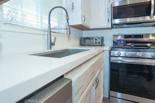 kitchen with a toaster, appliances with stainless steel finishes, a sink, and light countertops