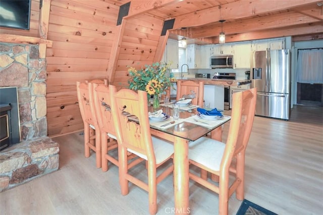 dining area with beamed ceiling, light wood finished floors, and wood walls