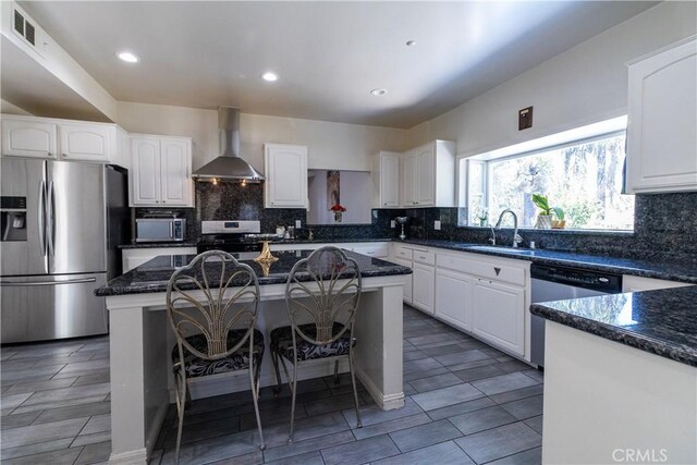 kitchen featuring visible vents, a breakfast bar, wall chimney exhaust hood, a sink, and stainless steel appliances