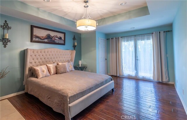 bedroom with baseboards, a tray ceiling, and hardwood / wood-style flooring