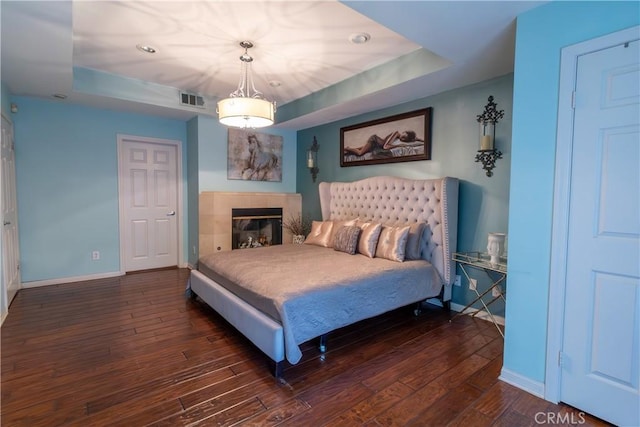 bedroom with dark wood-style flooring, recessed lighting, baseboards, a tray ceiling, and visible vents
