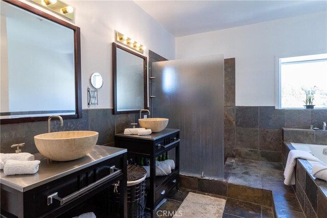 full bath with a garden tub, a sink, two vanities, and tile walls