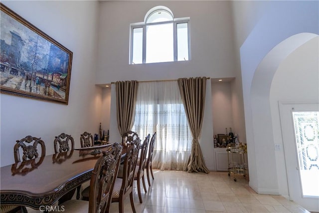 dining space with light tile patterned floors, arched walkways, a wealth of natural light, and a towering ceiling