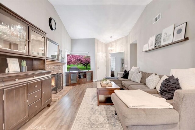 10830 Sundance Dr, Rancho Cucamonga, CA 91730 - living room with a brick fireplace, light wood-style flooring, visible vents, and high vaulted ceiling