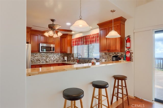 kitchen with stainless steel microwave, a peninsula, freestanding refrigerator, and decorative backsplash