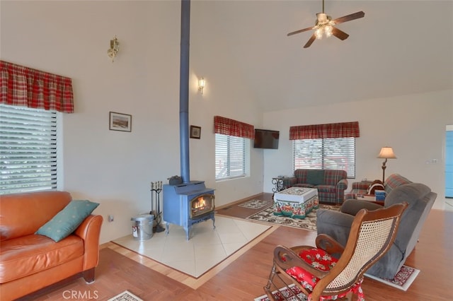 living area with wood finished floors, ceiling fan, high vaulted ceiling, and a wood stove