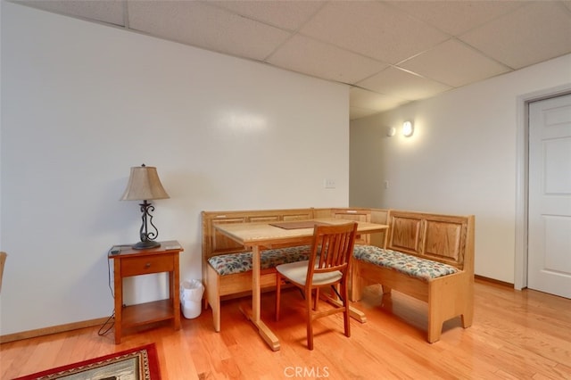dining area featuring baseboards, light wood-type flooring, breakfast area, and a paneled ceiling