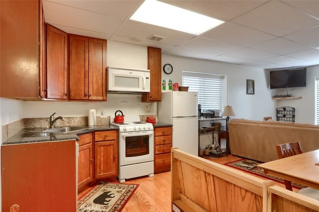kitchen featuring brown cabinets, a sink, dark countertops, a drop ceiling, and white appliances