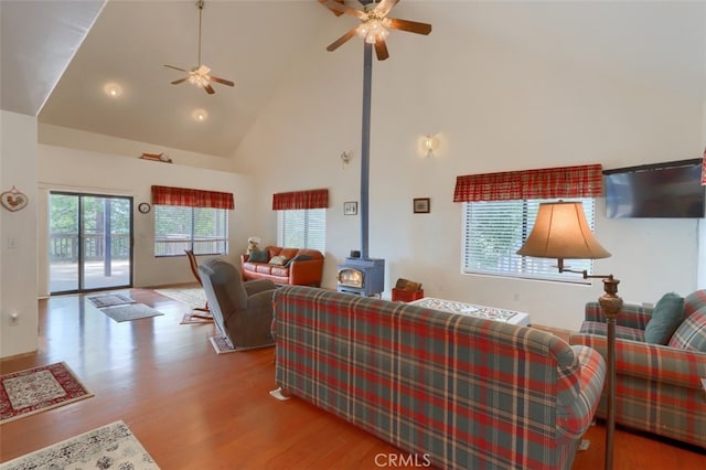 living room featuring wood finished floors, ceiling fan, high vaulted ceiling, and a wood stove