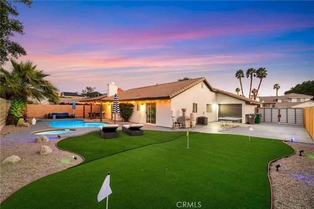 back of property at dusk with a patio area, a fenced backyard, cooling unit, a fenced in pool, and an in ground hot tub