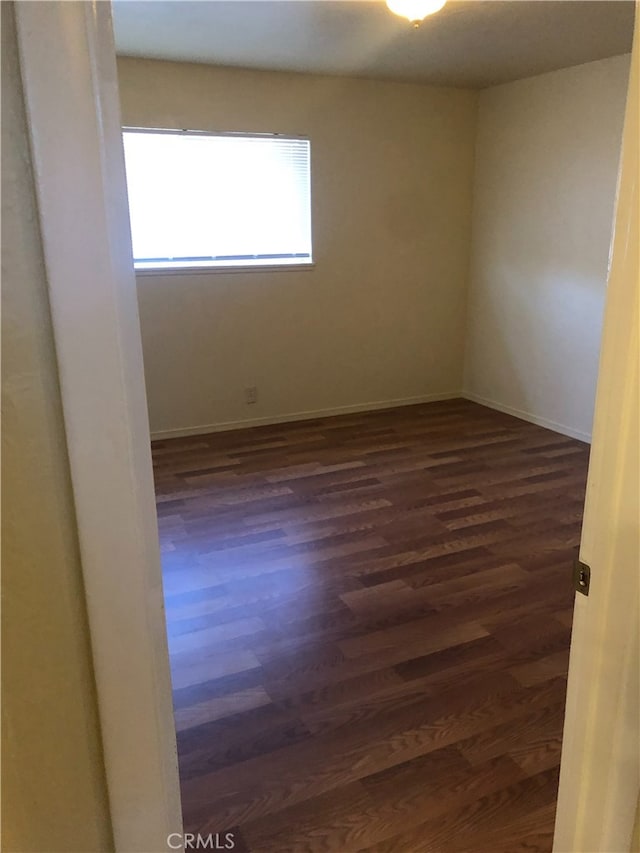 unfurnished room with baseboards and dark wood-style flooring