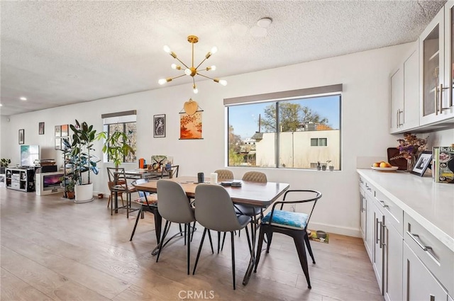 dining space with plenty of natural light, a textured ceiling, light wood finished floors, and an inviting chandelier