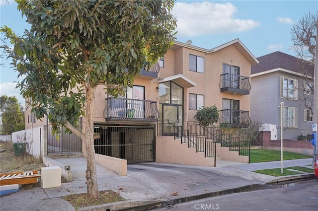 view of front of property with stairway, a gate, fence, a balcony, and stucco siding