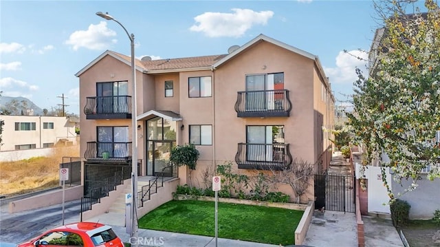 view of property featuring stucco siding, a gate, fence, and a balcony