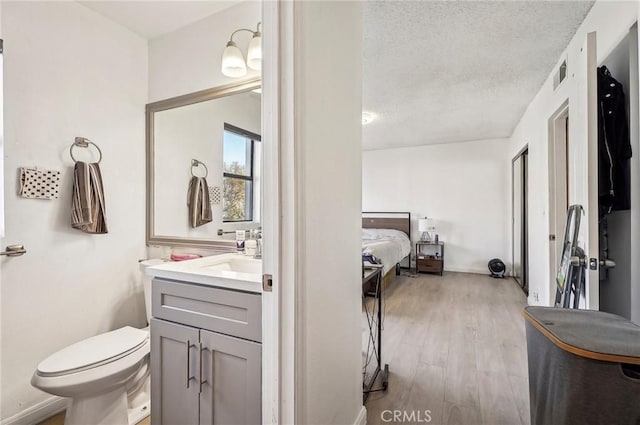 ensuite bathroom with wood finished floors, ensuite bathroom, vanity, toilet, and visible vents