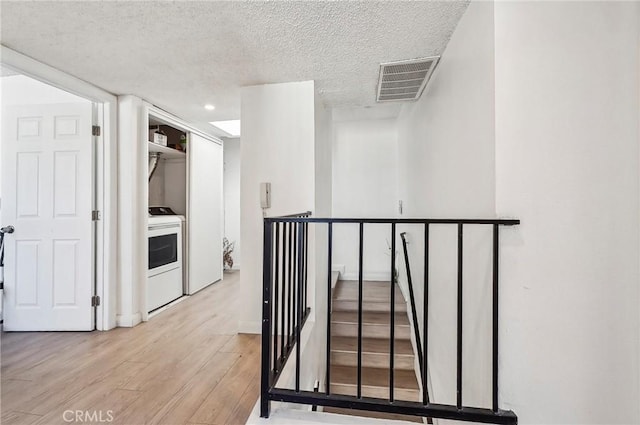 corridor with wood finished floors, visible vents, a textured ceiling, and an upstairs landing
