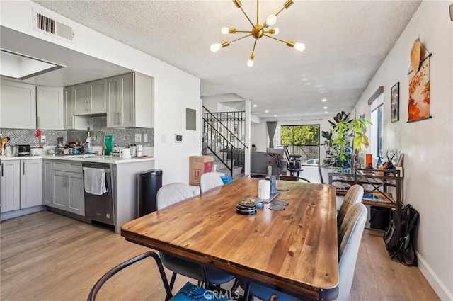 dining room with stairway, a textured ceiling, a chandelier, light wood-style flooring, and visible vents