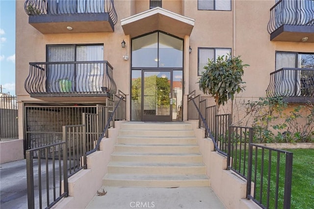 view of exterior entry with a balcony and stucco siding