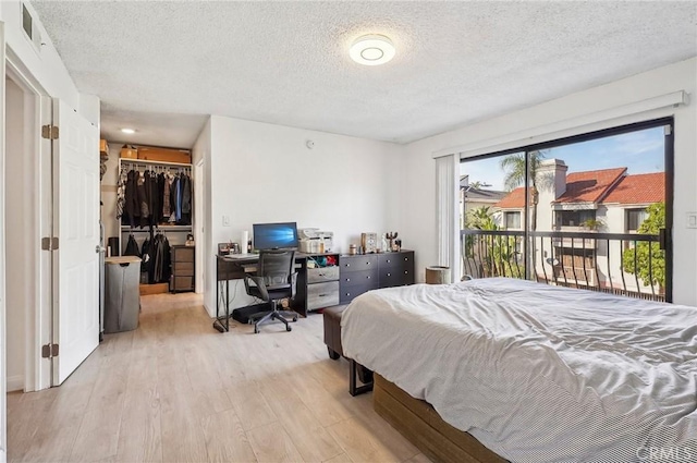 bedroom with a textured ceiling, visible vents, wood finished floors, access to outside, and a walk in closet