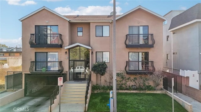 multi unit property with stucco siding, a balcony, and fence