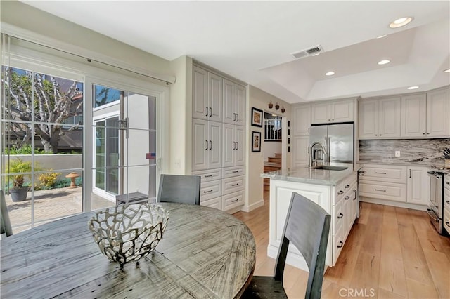 kitchen featuring an island with sink, light stone counters, visible vents, light wood-type flooring, and stainless steel refrigerator with ice dispenser