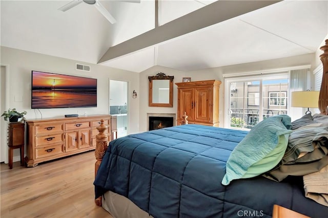 bedroom featuring a glass covered fireplace, vaulted ceiling with beams, visible vents, and light wood-style flooring