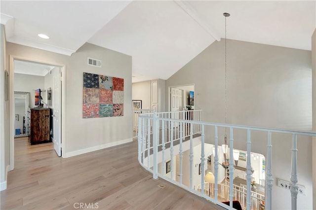 hallway featuring light wood finished floors, visible vents, an upstairs landing, beam ceiling, and baseboards