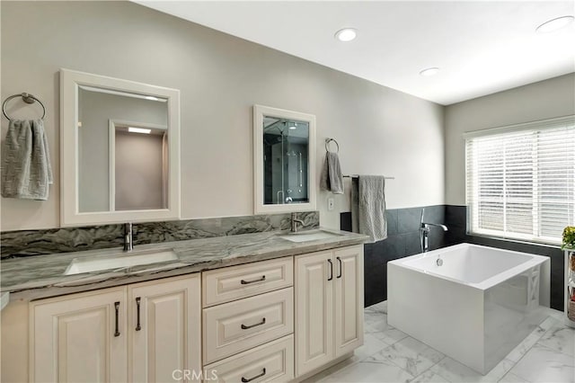 full bathroom featuring marble finish floor, a soaking tub, a sink, and double vanity