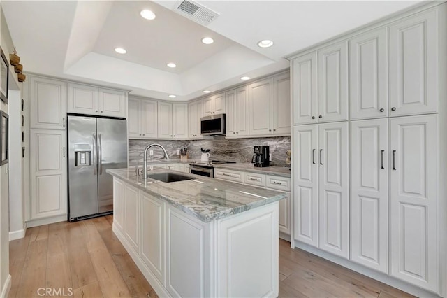 kitchen featuring a sink, light wood-type flooring, a tray ceiling, appliances with stainless steel finishes, and visible vents